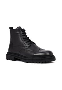 Zwarte leren enkelboot met vetersluiting, brogue-details, gestructureerd leer, verstevigde rubberen zool en een trekhaak aan de achterkant.