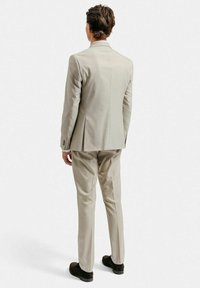 Beige kostym med en figursydd jacka och raka byxor. Tyget har en slät yta. Har en enda slits och två knappar på ärmarna.