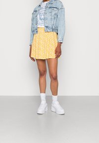 Denim takki; valkoinen graafinen t-paita; keltainen kukkakuosiset hame; valkoiset chunky-tennarit; valkoiset sukat. Yksinkertainen ja rento asu.