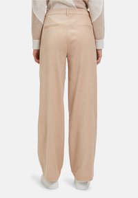 Lichtbeige corduroybroek met wijde pijpen, subtiele verticale strepen en twee achterzakken, gedragen met witte sneakers.