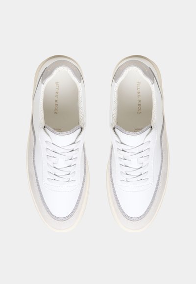 Et par hvite og lysegrå lave sneakers med lisser, sett ovenfra på en ensfarget lys bakgrunn.