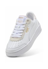 Valkoinen nahkainen lenkkari, jossa on rei'itetty varvasosa, beige yksityiskohtia, litteät valkoiset nauhat, kultainen logo sivulla ja kielellä, paksu valkoinen pohja, jossa on karhea pinta.