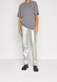 Šedé oversized tričko s viditelnou texturou, spárované s lesklými stříbrnými fitted kalhotami a černými robustními botami. Jednoduchý design a barvy.