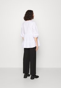 Valge peplum pluus puffed sleeves'iga, millel on volangserv, koos mustade laia jala pükste ja massiivsete mustade kingadega.