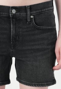 Čierne džínsové kraťasy so priliehavým strihom, s piatimi vreckami, zapínaním na gombík a zips a jemným opotrebením pozdĺž okrajov.