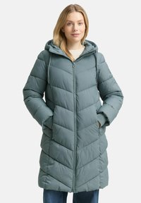 Teal pufferjack met een rits aan de voorkant, een capuchon en zijzakken. Kenmerkt zich door horizontale chevronstiksels en ribgebreide manchetten voor extra warmte.