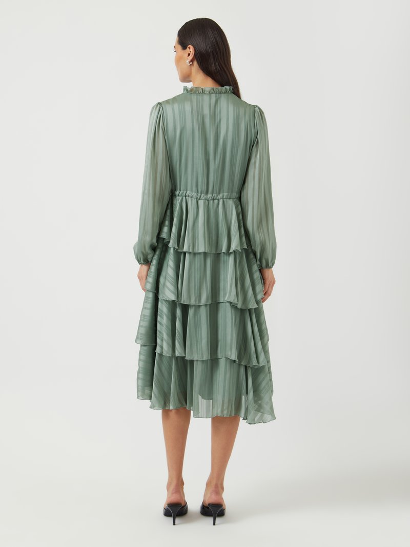 Grünes, plissiertes Kleid mit langen Ärmeln und einem Rüschenausschnitt, das einen gestuften Rock und eine taillierte Taille aufweist und mit schwarzen High Heels getragen wird.