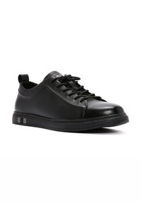 Sneaker in pelle nera con punta tondeggiante, profilo basso, design con lacci e dettagli a contrasto sul tallone e sulla suola.