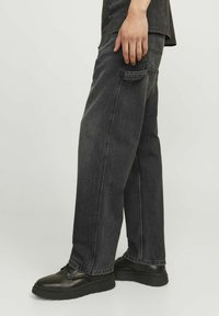 Svarta denimjeans med en avslappnad passform, med sidoficka, kontrasterande sömmar och uppvikta fållar, i kombination med kraftiga svarta skor.