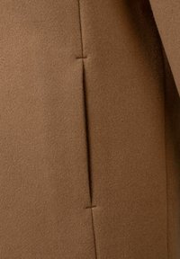 Pruun villakangas, millel on pehme tekstuur ja nähtavad õmblused ning peen õmblusdetail. Pind on sile ja sooja tooni.