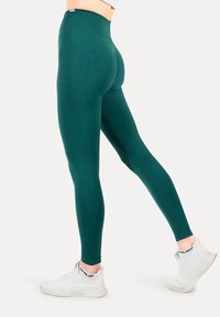 Leggings verdi realizzati in un tessuto elastico con vita alta e design senza cuciture, abbinati a scarpe da ginnastica bianche.