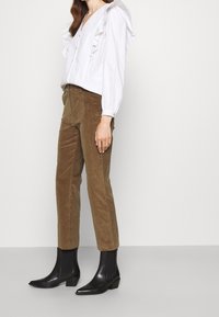 Witte blouse met gerimpelde details, gecombineerd met bruine corduroy broek. Zwarte enkellaarsjes met een puntige neus en blokhak.