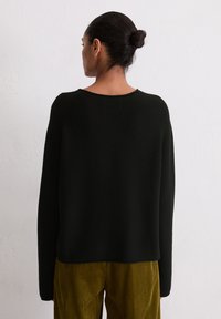 Schwarzer, gestrickter Pullover mit lockerer Passform und weitem Ausschnitt, kombiniert mit olivgrünen Cordhosen. Glatte Textur, schlichtes Design.