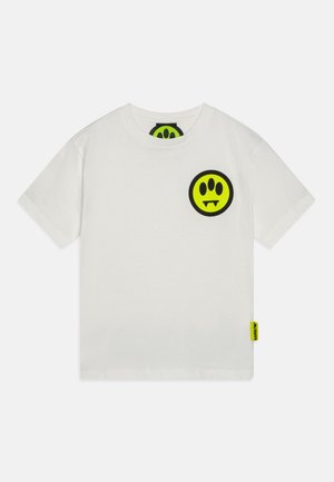 Hvid T-shirt med korte ærmer, rund halsudskæring og et lille neon-gult og sort smileylogo med hugtænder på øverste venstre side af brystet.