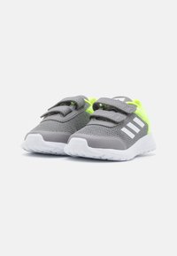 Zapatillas deportivas grises con tela de malla, acentos en neón verde y suela blanca. Cuentan con correas de Velcro y tres franjas blancas en el lateral.