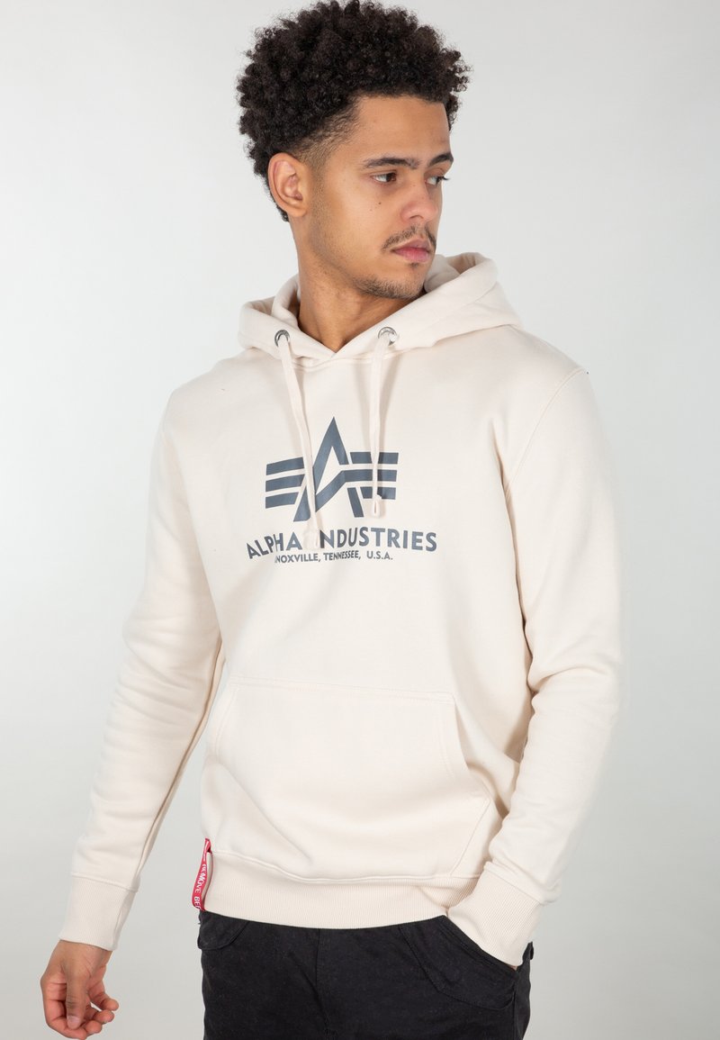 Felpa beige con tasca frontale, cappuccio con cordino e stampa del logo in grigio scuro. Polsini e orlo a coste, con un’etichetta di accentuazione rossa.