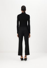 Black long-sleeve top with fitted design and high collar, paired with black wide-leg trousers and open-toe heeled shoes.