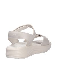 Sandalia de cuero beige con una suela acolchada, que cuenta con correas ajustables y un diseño abierto. Superficie texturizada; tacón de cuña elevado.