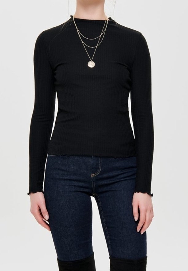 Haut noir côtelé à manches longues avec un col montant, assorti à un jean bleu foncé. Comprend des colliers dorés superposés et des bords de manches effilochés.