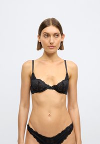 Czarny koronkowy biustonosz z fiszbinami i regulowanymi ramiączkami. Ozdobiony kwiatowymi wzorami i falistymi brzegami. Do kompletu dopasowane koronkowe majtki.