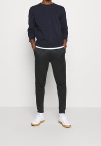 Marinblå sweatshirt med rund hals, långa ärmar och ribbade manschetter, ihopparad med svarta tapered-byxor och vita sneakers. Slät tyg, avslappnad passform.