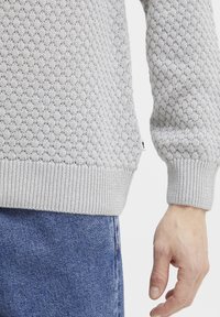 Pulover tricotat de culoare gri deschis, având un model texturat în formă de diamant. Mansetele și tivul din tricot cu nervuri oferă un contrast față de materialul principal.