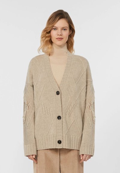 Cardigan en maille beige avec un col en V, présentant des motifs texturés, une fermeture à boutons et des détails à franges sur les manches.