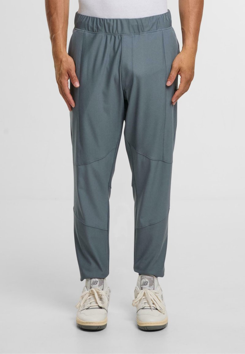 Grå träningstights med elastisk midja, avsmalnande design och sidoseamdetaljer; bärs med vita sneakers.