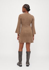 Robe pull marron à côtes avec des manches longues évasées, une silhouette ajustée et une longueur au-dessus du genou, associée à des bottes grises jusqu'aux genoux.