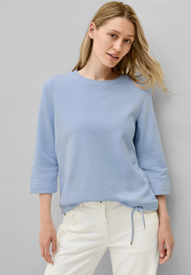 Sweatshirt en coton bleu clair avec un col rond, des manches trois-quarts et un ourlet à cordon de serrage. Assorti à un pantalon blanc.