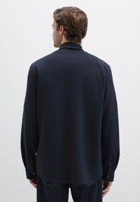 Marineblaues Langarmhemd mit lockerer Passform, glatter Textur, geknöpften Manschetten und klassischem Kragen, kombiniert mit dunklen Jeans.