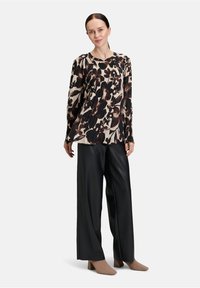 Maglietta a maniche lunghe con stampa floreale in nero, marrone e beige, abbinata a pantaloni larghi neri e scarpe con tacco beige.