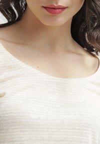 Beżowy, lekki materiał z drobnymi, poziomymi paskami. Dekolt w serek i gładka tekstura. Bluzka dopasowana do ciała, bez wzorów i ozdób.