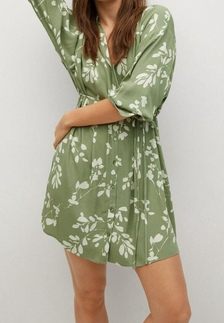 Vestido floral verde hecho de tela ligera. Cuenta con mangas cortas, diseño cruzado y patrones de hojas blancas por todo el vestido.