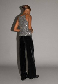 Trblietavý strieborný top bez rukávov s tenkými ramienkami, doplnený o široké nohavice z čierneho zamatu. Tento outfit sa vyznačuje hladkou textúrou a elegantným strihom.