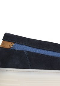Scarpa in suede blu navy con una striscia in tela blu, accento in pelle beige e suola in gomma bianca. Presenta cuciture lungo il bordo.
