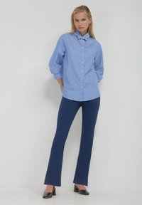 Blau-weiß gestreiftes Hemd mit Knopfleiste und Kragen, kombiniert mit marineblauen Schlaghosen und schwarzen High Heels. Glatte Texturen und taillierte Passform.