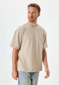 Beige struktureret kortærmet t-shirt med rund hals og afslappet fit, parret med lyseblå denim jeans.