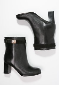 Botines de cuero negro con textura lisa, tacones altos de bloque, puño de gamuza y una banda con acento metálico.