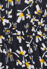 Tela marina con patrones geométricos en blanco, amarillo y azul, que presenta una cinturilla elástica y una superficie texturizada.