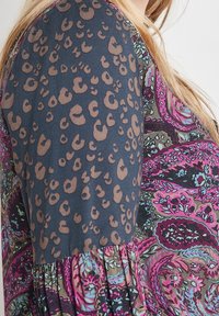 Flerfärgad blus med en mörk bakgrund och bruna leopardfläckar samt ett livligt paisley-mönster i rosa, blå och gröna nyanser.