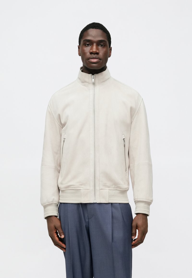 Veste zippée beige clair en matière douce avec poignets et ourlet côtelés, dotée de deux poches latérales et d'un col montant.