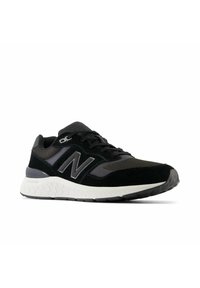 Baskets New Balance noires et grises avec lacets noirs, tige en mesh et en daim, semelle intermédiaire blanche texturée et semelle extérieure noire à motifs.