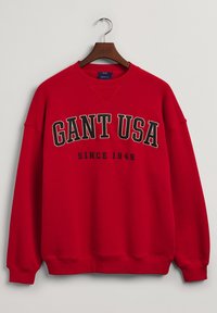Sudadera roja con cuello redondo, mangas largas y un corte relajado. Presenta el texto "GANT USA" y "SINCE 1949" en negro contrastante.