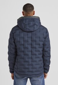 Marineblaue Steppjacke mit einem gesteppten Design und einer Kapuze, ausgestattet mit einem grauen Innenkragen. Glatte Textur, mittellange Passform und lange Ärmel.