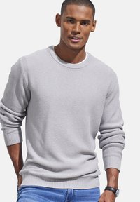 Hellgrauer strukturierter Pullover mit Rundhalsausschnitt und gerippten Bündchen, getragen mit blauen Jeans. Der Stoff hat ein gewebtes Muster.