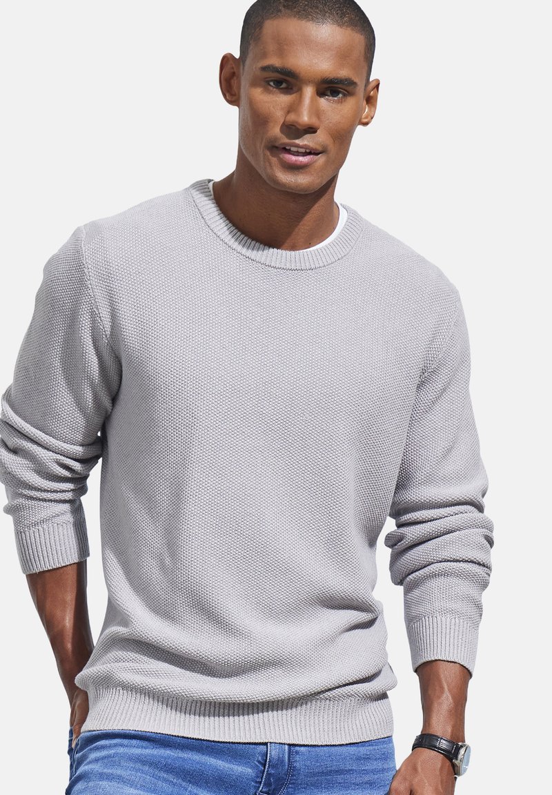 Hellgrauer strukturierter Pullover mit Rundhalsausschnitt und gerippten Bündchen, getragen mit blauen Jeans. Der Stoff hat ein gewebtes Muster.
