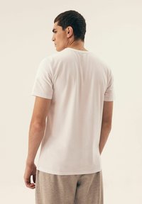 Biała koszulka z krótkim rękawem, wykonana z miękkiej bawełny, z okrągłym dekoltem i gładką strukturą, pokazana z tyłu na neutralnym tle.