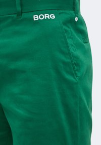 Πράσινο παντελόνι με πλαϊνές τσέπες που φέρουν λευκό κεντητό κείμενο "BORG" και ένα μικρό εικονίδιο τενιστικής μπάλας κοντά στην άκρη της τσέπης.
