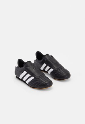 Par de zapatillas Adidas de cuero negro con rayas blancas, cierre de velcro y puntera texturizada sobre un fondo blanco.